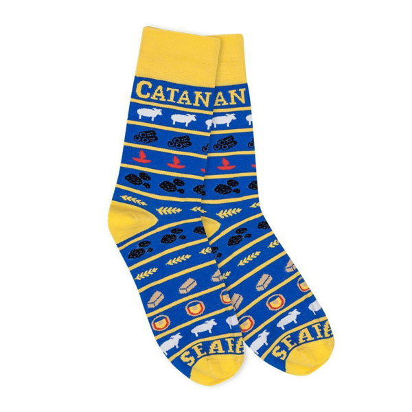 Blue and yellow socks written Catan in yellow at the top with illustrations of wheat, sheeps, wood and birds all over it