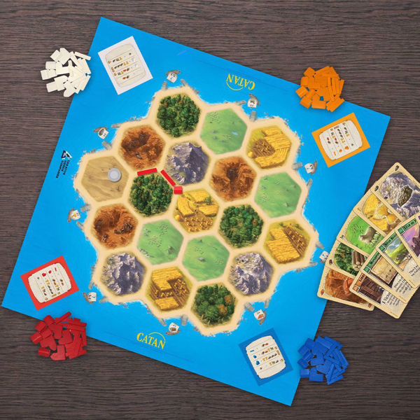 Board of the game Catan Play Board  flat on the ground, surrounded by the game's cards and pieces